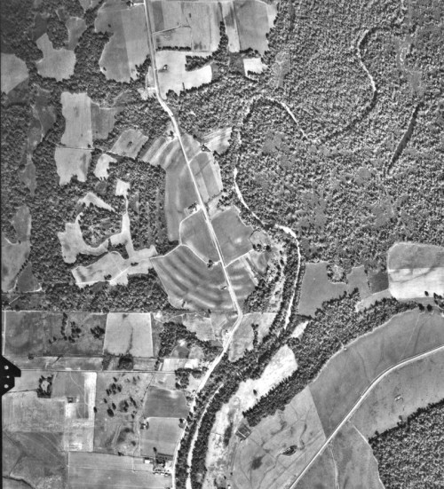 Aerial view of a rural landscape featuring fields, roads, and patches of forest along a winding river.