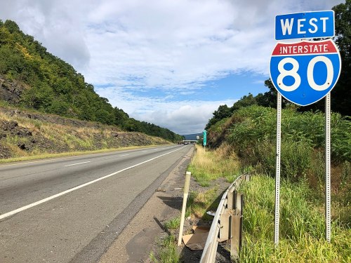 A highway sign for Interstate 80 West, with a view of the road and greenery along the roadside.