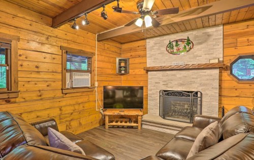 Cozy cabin living room with wooden walls, a stone fireplace, TV, and comfortable seating.