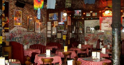 Cozy restaurant interior with red-checkered tables, brick walls, and eclectic decor, including graffiti and colorful lights.