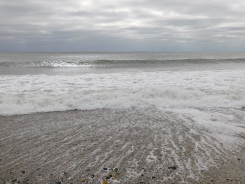 Waves gently roll onto a sandy beach under a cloudy sky, creating a serene coastal scene.