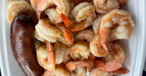 A close-up of cooked shrimp and a sausage in a white takeout container.