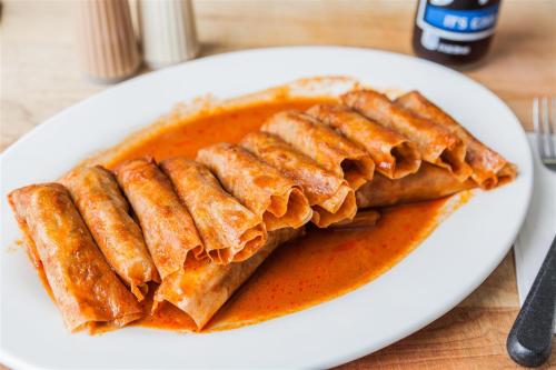 A platter of rolled enchiladas covered in red sauce, served on a white plate with a wooden table background.