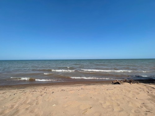 A serene beach scene with gentle waves lapping at the sandy shore under a clear blue sky.