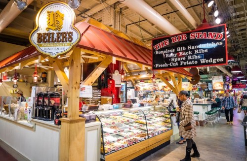 A bustling market stall featuring doughnuts and a rib stand with a menu of various rib dishes and sides.