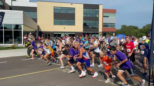A large group of runners of all ages starts a race outside a modern building on a sunny day.