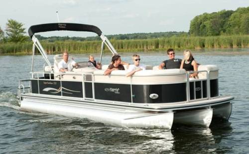 A group of people enjoying a sunny day on a pontoon boat on a lake, surrounded by greenery.