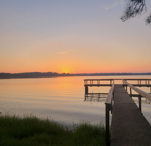 A serene lake at sunset, with a wooden dock extending into the calm water and a colorful sky in the background.