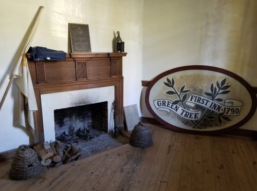 A rustic room featuring a wooden fireplace, a large sign reading "GREEN TREE," and historical artifacts.