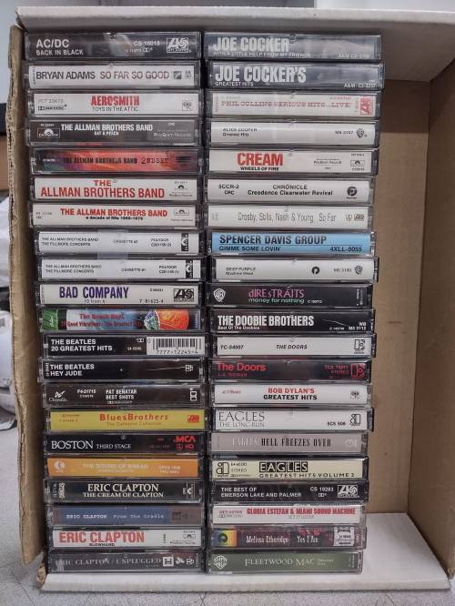 A box filled with various cassette tapes from artists like AC/DC, Joe Cocker, and The Allman Brothers Band.