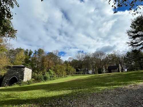 A grassy area with trees and two rustic buildings under a partly cloudy sky.