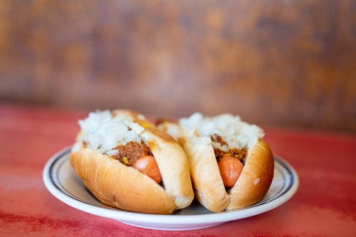 Two hot dogs in buns topped with chopped onions, served on a plate against a colorful background.