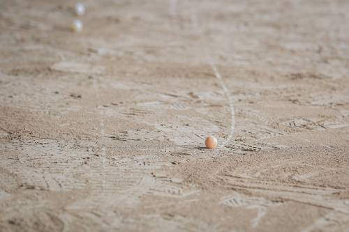A close-up of a sandy surface with a single ball and faint chalk lines marking a path.