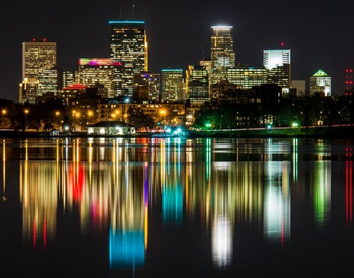 City skyline at night reflecting in water, with colorful lights illuminating buildings and a serene atmosphere.