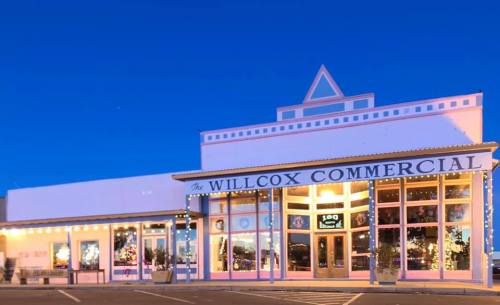 Historic building with "Willcox Commercial" sign, featuring large windows and decorative lights, under a twilight sky.