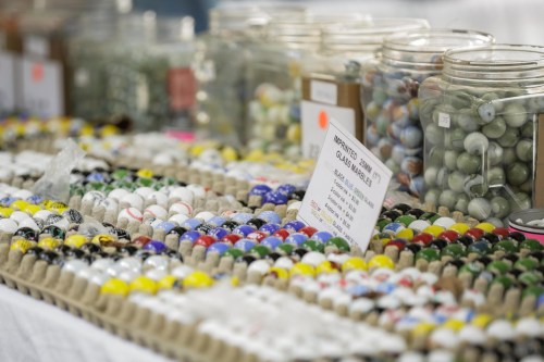 A colorful display of marbles in jars and trays at a market, with a sign indicating prices and types.