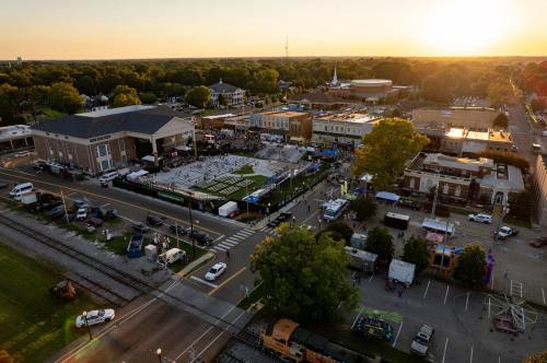 Aerial view of a bustling outdoor event with a sports field, surrounded by buildings and trees at sunset.