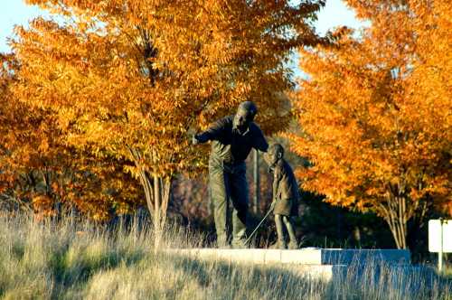 A bronze statue of a man and a child, surrounded by vibrant autumn trees with orange leaves.