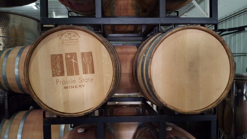 Two wooden wine barrels stacked on a rack, featuring the logo of Prairie State Winery.