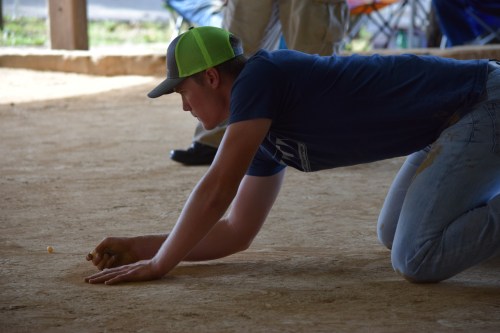 A young man in a blue shirt and green cap kneels on the ground, focused on a small object in front of him.