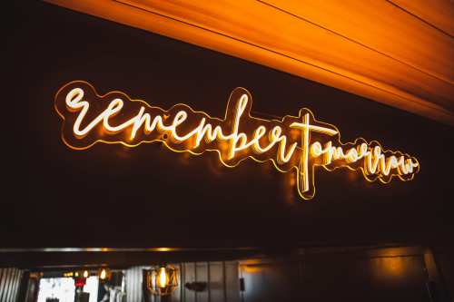 Neon sign reading "remember tomorrow" illuminated against a dark wall in a cozy setting.
