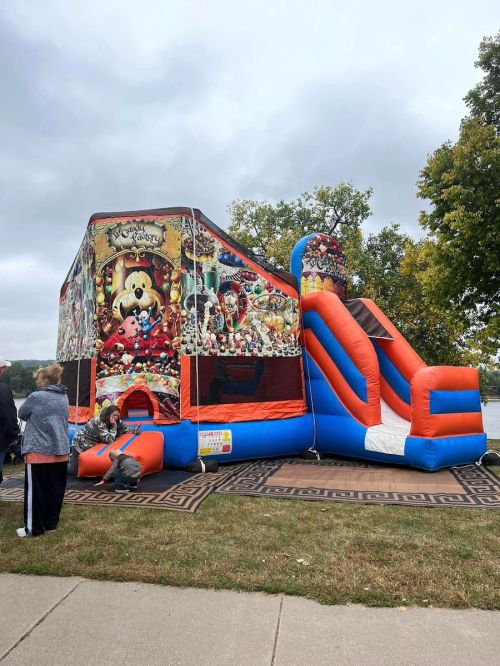 A colorful inflatable bounce house with a slide, set up near a lake, with people nearby enjoying the attraction.