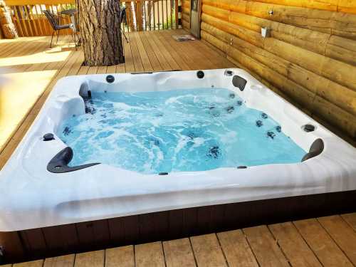 A hot tub filled with water, surrounded by wooden decking and a rustic log cabin backdrop.