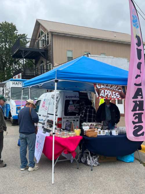 A vendor tent with a blue canopy, selling caramel apples and treats, with customers browsing nearby.