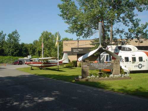 Aviation Hall of Fame entrance with a small plane and helicopter displayed outside, surrounded by trees and flags.