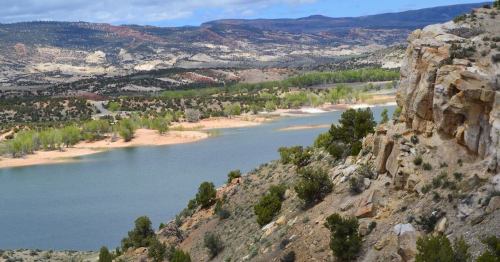 A scenic view of a river winding through green trees and rocky hills under a partly cloudy sky.
