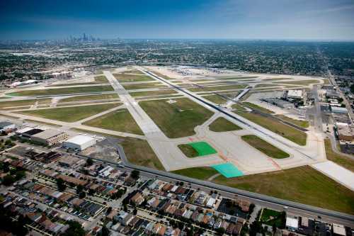 Aerial view of an airport with runways, taxiways, and surrounding urban landscape under a clear blue sky.