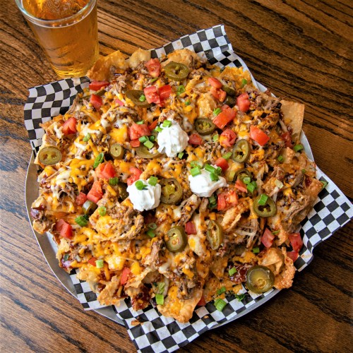 A large plate of nachos topped with cheese, jalapeños, tomatoes, sour cream, and green onions, with a drink beside it.