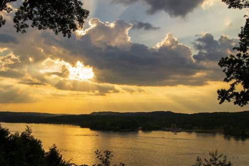 Sunset over a tranquil lake, with golden rays breaking through clouds and reflecting on the water's surface.