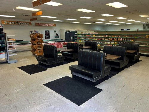 Empty diner interior with black booths, tables, and shelves stocked with various food items. Brightly lit and spacious.