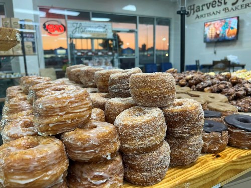 A display of assorted donuts, including glazed and chocolate varieties, in a bakery with a sunset view in the background.