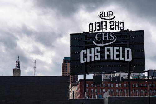 Sign for CHS Field against a cloudy sky, with city buildings visible in the background.