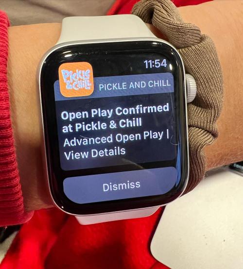 A smartwatch displays a notification for "Open Play Confirmed at Pickle & Chill" with options to view details or dismiss.