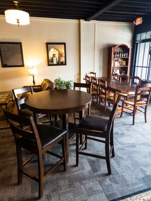 A cozy dining area with wooden tables and chairs, featuring a plant and soft lighting.