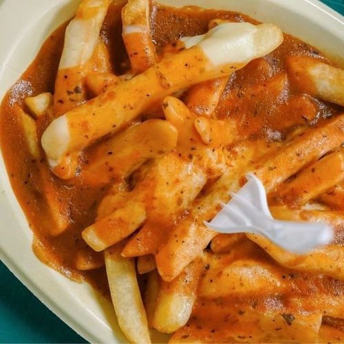 A close-up of fries topped with a rich, orange gravy and melted cheese, served in a white container.
