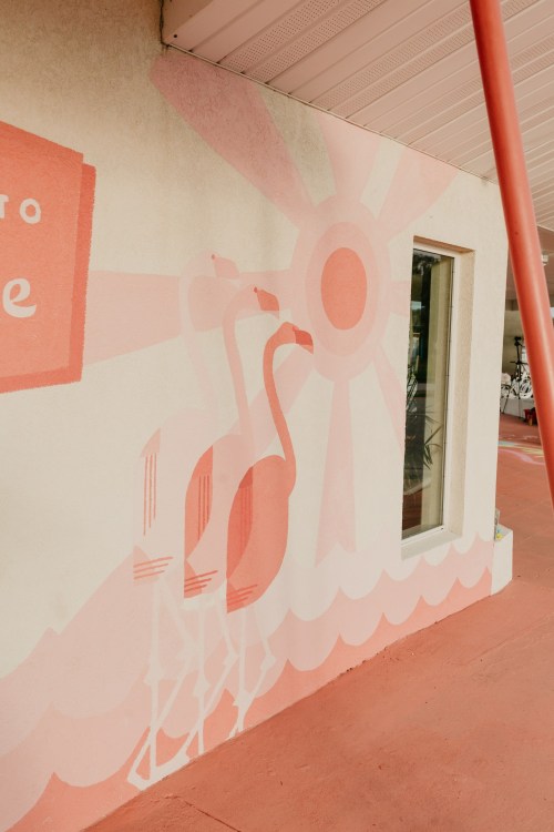 A mural featuring pink flamingos and a sun on a light-colored wall, with a red floor beneath.