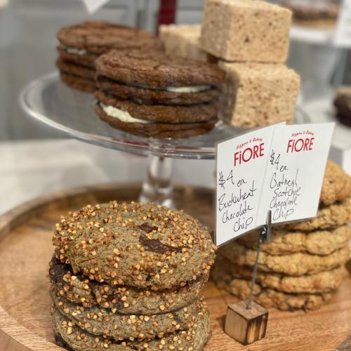 A display of cookies and rice treats on a wooden platter, with price tags for buckwheat chocolate chip cookies.