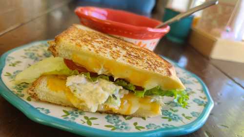 A grilled cheese sandwich with lettuce and tomato on a decorative plate, alongside a small bowl.