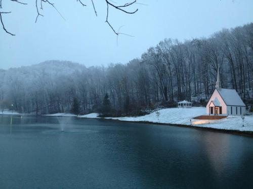 A serene winter scene featuring a small white chapel by a snowy lake, surrounded by trees and a gentle mist.