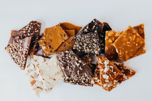 A variety of chocolate bark pieces topped with nuts and caramel, arranged on a white background.