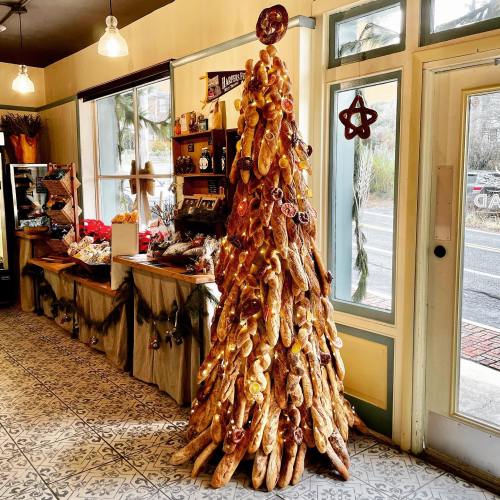 A unique Christmas tree made of bread and pastries, decorated with colorful ornaments, inside a cozy shop.