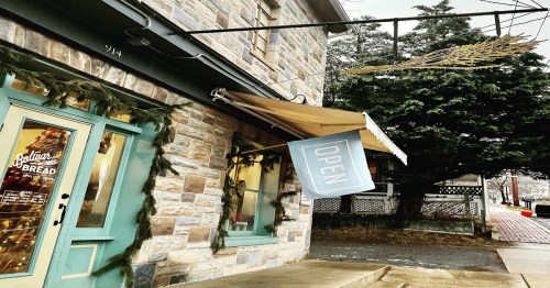 A stone building with a blue "OPEN" sign and festive decorations, surrounded by greenery and a wintery atmosphere.