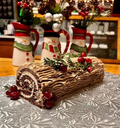 A festive yule log cake decorated with berries and greenery, set against a backdrop of snowman-themed pitchers.