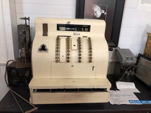 An old-fashioned cash register with buttons and a display, placed on a table among vintage items.