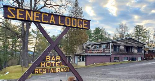 Sign for Seneca Lodge with bar, motel, and restaurant; rustic building in the background surrounded by trees.
