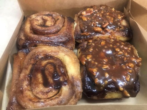 A box containing two cinnamon rolls, one plain and one topped with caramel and nuts.